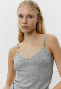 Siva pletena majica na bretele s tankim trakama i V-izrezom. Ima suptilnu vertikalnu rebrastu teksturu i uski dizajn.