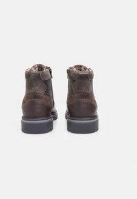 Botine din suede și piele de culoare maro, până la gleznă, cu închidere prin fermoar, detalii texturate și talpă din cauciuc. Interiorul are un căptușeală cu un model.