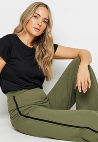 T-shirt nero a maniche corte abbinato a pantaloni verdi oliva a vita alta con strisce laterali nere e un tessuto liscio e testurizzato.