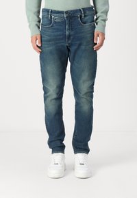 Light blue denim jeans with a straight fit, faded details on the thighs, five-pocket design, and silver hardware. Worn with white sneakers.