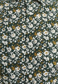 Květinová košile se zeleným pozadím, na které se nachází bílé a hořčičně žluté květiny. Zapínání na knoflíky vpředu s texturovaným povrchem.