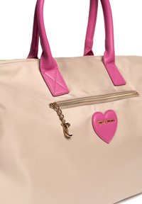 Beige Nylonhandtasche mit pinken Ledergriffen, einer Front-Reißverschlusstasche und einem pinken Herz-Akzent mit goldener Schrift und einem dekorativen Anhänger.