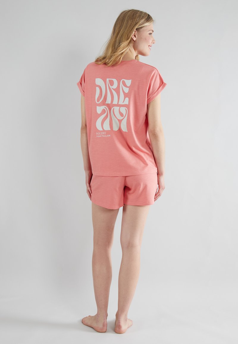 Růžový loungewear set obsahující volné tričko s velkým bílým nápisem "DREAM" a odpovídající šortky s uvolněným střihem a měkkou texturou.