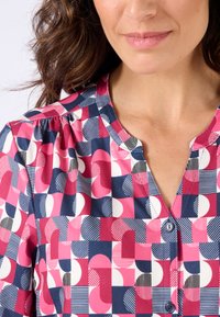 Camisa de botones con un patrón geométrico en rosa, azul marino y blanco. Tejido suave, escote redondo y mangas cortas con sutiles frunces.