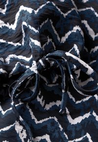 Tessuto blu e nero con motivo a zigzag. Presenta dettagli bianchi e un laccetto arricciato, realizzato in materiale leggero e testurizzato.