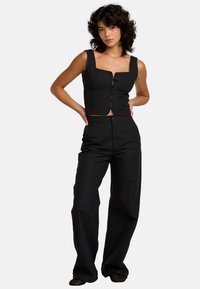 Zwarte crop top met vierkante halslijn en knopen aan de voorkant, gecombineerd met losse zwarte wijde broek. Glad textuur, minimalistisch ontwerp.
