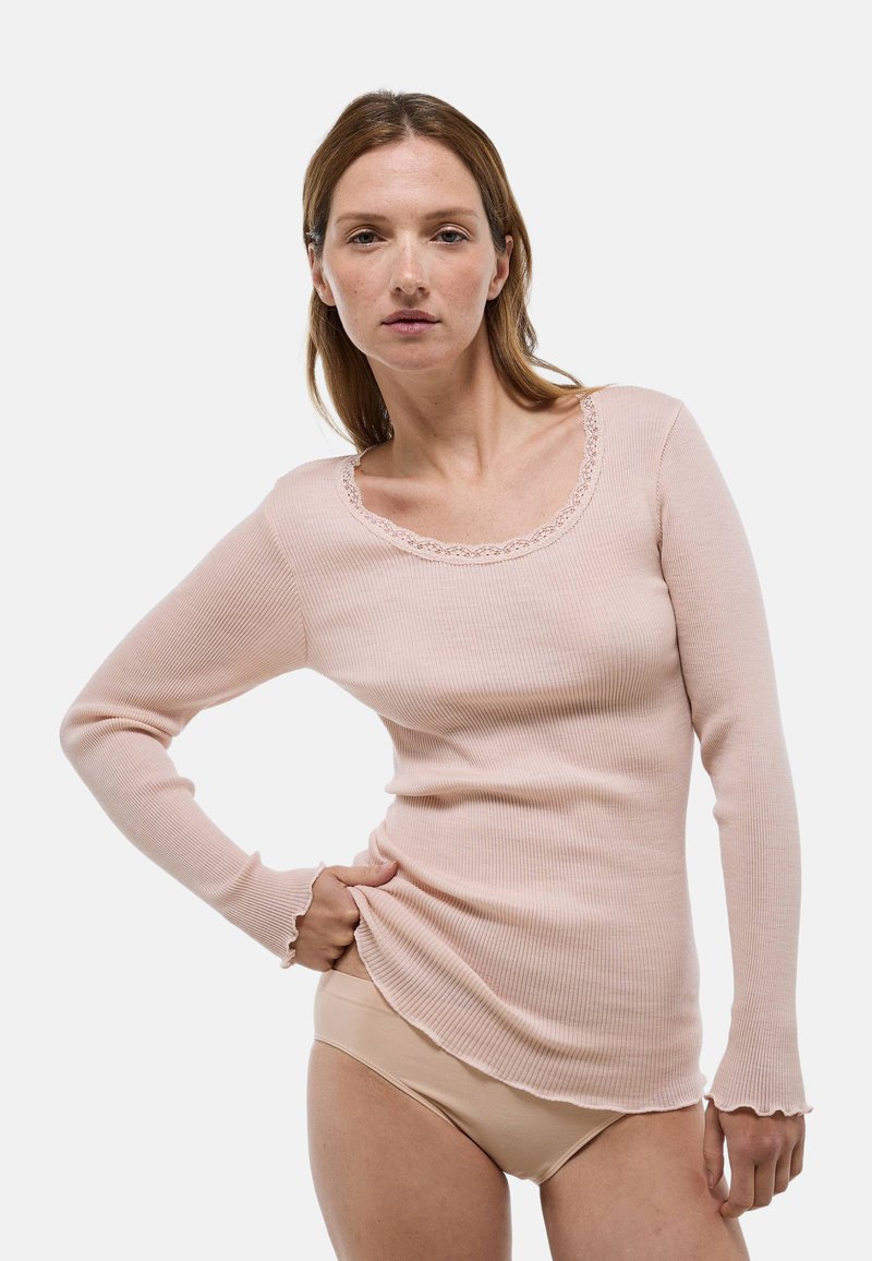 Pull à manches longues en maille côtelée rose clair avec un col en dentelle festonné et un tissu texturé, porté sur des sous-vêtements nus, silhouette ajustée.