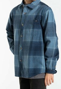 Koszula zapinana na guziki w niebieskim gradientowym wzorze w kratę. Posiada jasnoniebieskie i ciemnoniebieskie odcienie, długie rękawy oraz kieszeń na piersi z logo.