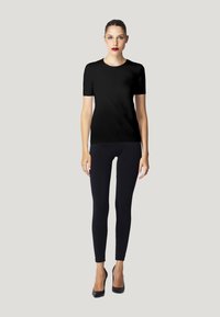 T-shirt noir à manches courtes associé à un legging noir. Le mannequin porte des escarpins noirs. Design simple et texture de tissu lisse.