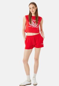 Top corto rojo con un estampado gráfico y pantalones cortos a juego. Material de mezcla de algodón, corte holgado, cintura elástica y bolsillos laterales. Zapatillas blancas con suelas ligeras.