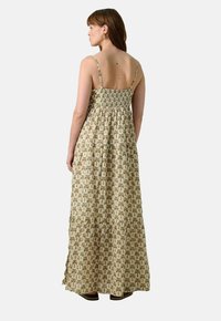 Robe maxi en tissu léger, avec un corsage smocké, des fines bretelles et un design à volants avec un motif de feuilles de palmier vertes et beiges.