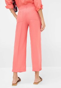 Wide-leg trousers in coral, made of textured fabric, featuring a high waistband and two back pockets. Hem ends just above the ankle.