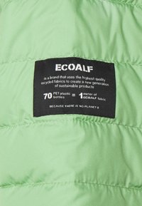 Green puffer fabric with a quilted texture. Black label with white text states environmental information and materials used in products.