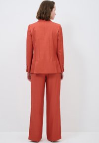 Rostvärgad blazer och matchande vida byxor. Blazern har en skräddarsydd passform, strukturerade axlar och bakseams. Slät textur.