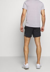 Camisa de manga corta gris claro con una textura sutil, combinada con pantalones cortos deportivos negros. Zapatillas blancas con detalles grises completan el conjunto.