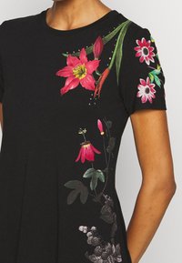 Schwarzes T-Shirt mit floraler Stickerei in lebendigen Farben, mit detaillierten Designs an den Ärmeln und der Vorderseite, die verschiedene florale Motive präsentieren.