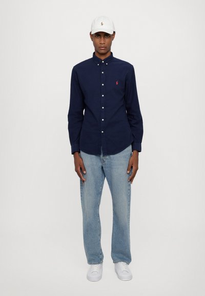 Marineblauw overhemd met knopen, lichtblauwe jeans, witte sneakers en een witte pet met logo. Casual outfit met een aansluitende pasvorm en gemaakt van katoen.