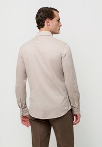 Beige shirt met lange mouwen, een platte kraag, mouwen met knopen en een gladde textuur. Voorzien van een gebogen zoom en een rugpasdetail.