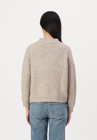 Beige wollen trui met een ronde hals en geribde manchetten. Losse pasvorm, textuur knit, gecombineerd met lichtblauwe denim. Minimalistisch ontwerp, zonder versieringen.
