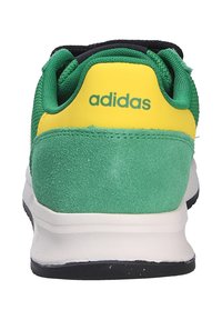 Sneaker Adidas verde e giallo vista da dietro, che mostra la texture scamosciata e la suola bianca con fondo nero.