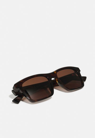 Occhiali da sole tartarugati con montatura quadrata e lenti marroni. Presentano cerniere laterali prominenti e una texture in plastica liscia.