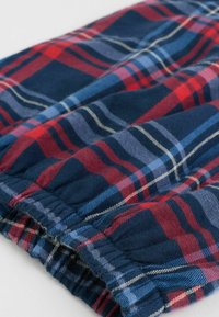 Tejido de algodón de cuadros con un fondo azul marino y rayas rojas, azules y blancas. Presenta una cinturilla elástica en el borde inferior.