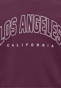 Tessuto marrone con grande testo bianco contornato "LOS ANGELES" che si inarca sopra un testo bianco più piccolo "CALIFORNIA".