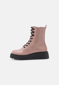 Bottines en cuir verni rose avec une semelle épaisse noire, dotées de lacets noirs et d'une languette à l'arrière. Fini lisse et brillant.