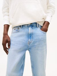 Jeans in denim blu chiaro con una vestibilità rilassata, design a cinque tasche e texture sbiadita, abbinati a una felpa con cappuccio di colore crema.