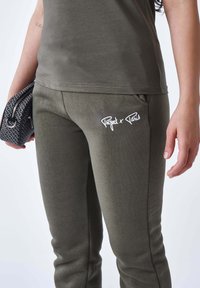 Pantalones de chándal verde oliva con una textura suave, que presentan un logo blanco "Project x Paris" en la pierna izquierda y bolsillos laterales.