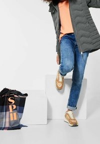 Grå puffjacka, orange topp, blå jeans, beige sneakers med vita accenter. Svart och blå rutig scarf med "SPIF" i orange bokstäver.