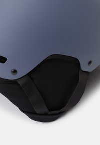 Matná námořnická modrá helma s černým textilním podšívkou, nastavitelným černým popruhem a ventilačními otvory. Disponuje pevným designem a elegantním povrchem.