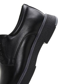 Zapato de cuero negro con diseño de caña alta, suela de goma texturizada y acabado suave. Cuenta con cierre de cordones y detalles de costura sutil.