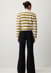 Gebreide jas met brede groene en witte strepen, een kraag en decoratieve knopen aan de onderkant; gecombineerd met wijd uitlopende zwarte broeken.