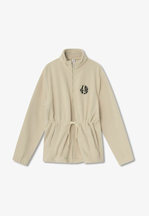 Beige színű polár zipzáras dzseki magas gallérral, állítható húzózsinórral a deréknál, két elülső zsebbel és fekete kör alakú logóval a bal oldalon.