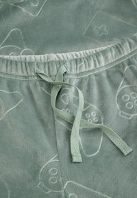 Jasnozielone, miękkie spodnie z polaru z elastycznym pasem i dopasowanym wiązaniem. Posiadają wytłoczone wzory w formie zabawnych kształtów i tekstur.