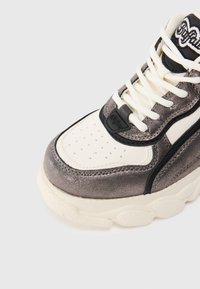 Masivní tenisky s kovovými stříbrnými svršky a krémovými akcenty. Obsahují černé detaily, perforovanou špičku a texturovanou podrážku. Pohled zvrchu.