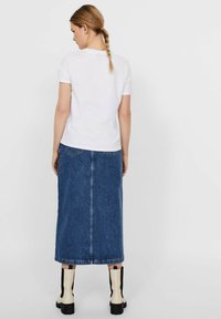 White cotton t-shirt paired with a blue denim maxi skirt. The skirt features two back pockets and a straight cut. Black and cream ankle boots.