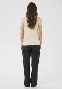 Světlá béžová blůza s krajkovými cap sleeve, spárovaná s černými širokými džínami. Hladká textura, minimalistický design a uvolněný střih.