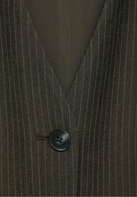 Dunkel gestreifter Stoff mit einem tiefen V-Ausschnitt. An der linken Seite befindet sich ein schwarzer Knopf, die Oberfläche hat eine strukturierte Textur mit subtiler glänzender Optik.