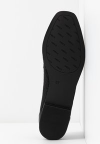 Suola di scarpa nera con un motivo testurizzato e bordi lisci, etichettata "37". Il lato interno presenta un design intrecciato, in contrasto con il materiale in gomma opaca.