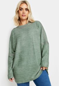 Olivgrön oversized sweatshirt i mjukt tyg, med båtformad halsringning och dekorativa metallspikar längs axlarna och ärmarna.