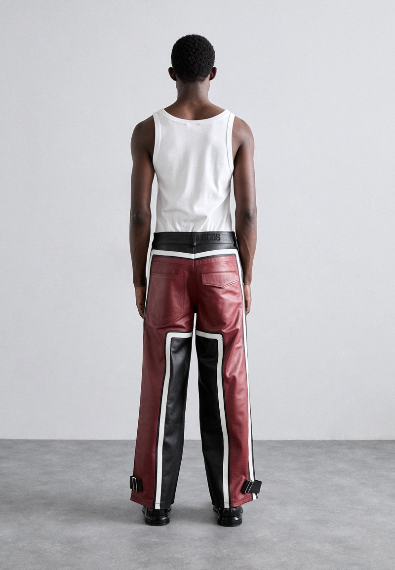 Pantalons en cuir rouge et noir avec des accents blancs, design à jambe large, détails matériels sur les côtés et une taille noire avec logo.