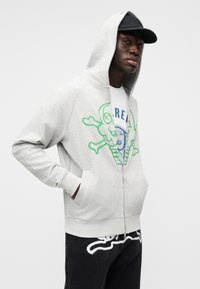 Ανοιχτό γκρι φούτερ με φερμουάρ με πολύχρωμο σχέδιο που απεικονίζει έναν κώνο παγωτού και έναν κρανίο. Ριμπ μανσέτες και τσέπη καγκουρό.