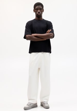 T-shirt noir à manches courtes, pantalon large blanc et baskets grises. Textures lisses, design simple et coupe décontractée.