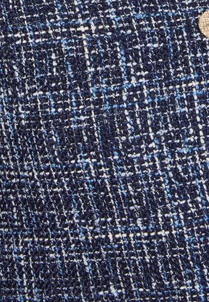 Marineblauwe geweven stof met een textuurpatroon, met door elkaar gevlochten draden in lichtere blauw- en crèmekleuren, en een ronde metalen accent.