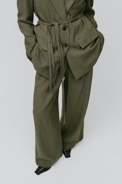 Costume oversize à carreaux vert olive avec blazer ceinturé et pantalon à jambes larges, associé à des chaussures noires à lacets pointues.