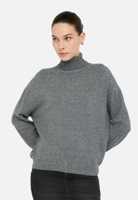 Grauer Rollkragenpullover mit lockerer Passform, geripptem Ausschnitt und dezent strukturiertem Strick. Mit überschnittenen Schultern und langen Ärmeln.