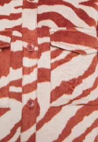 Veste en tissu doux à rayures zèbre rouges et blanches, dotée de deux poches poitrine à rabat avec boutons et de boutons rouges sur le devant.