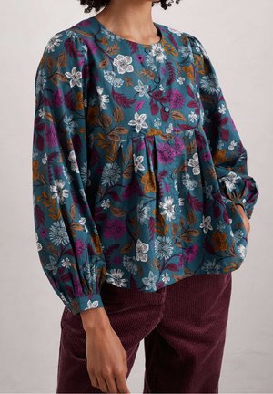 Bluse i grønblå med blomster i lilla, hvid og brun, med knaplukning foran, puffede lange ærmer, kombineret med bordeauxfarvede bukser i kordfløjl.